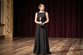 Actrice oscarisée tenant une statuette dorée sur une scène de théâtre avec des rideaux en velours et un parquet en bois